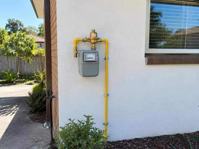 Gas meter and yellow gas piping on an exterior brick-and-render wall in a suburban yard in St Ives