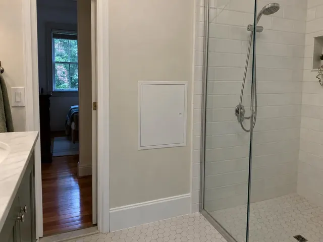 Bathroom wall with a small access panel beside a tiled shower and timber hallway in Pymble